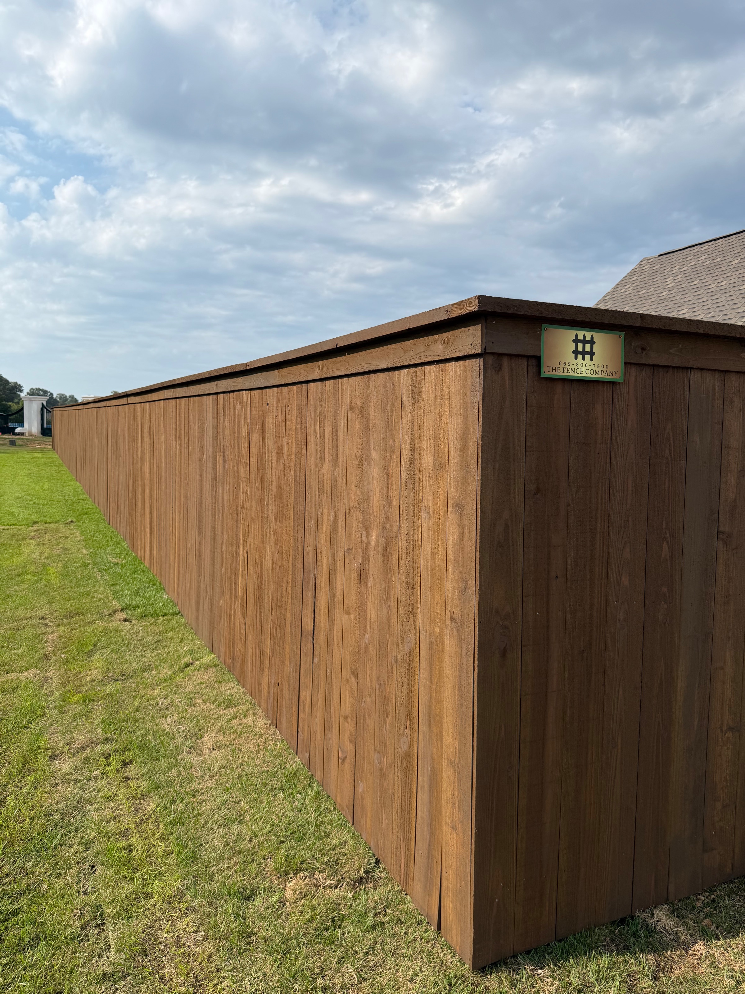 Pre-stained cedar privacy fence with a finished cap board and a The Fence Company yard sign