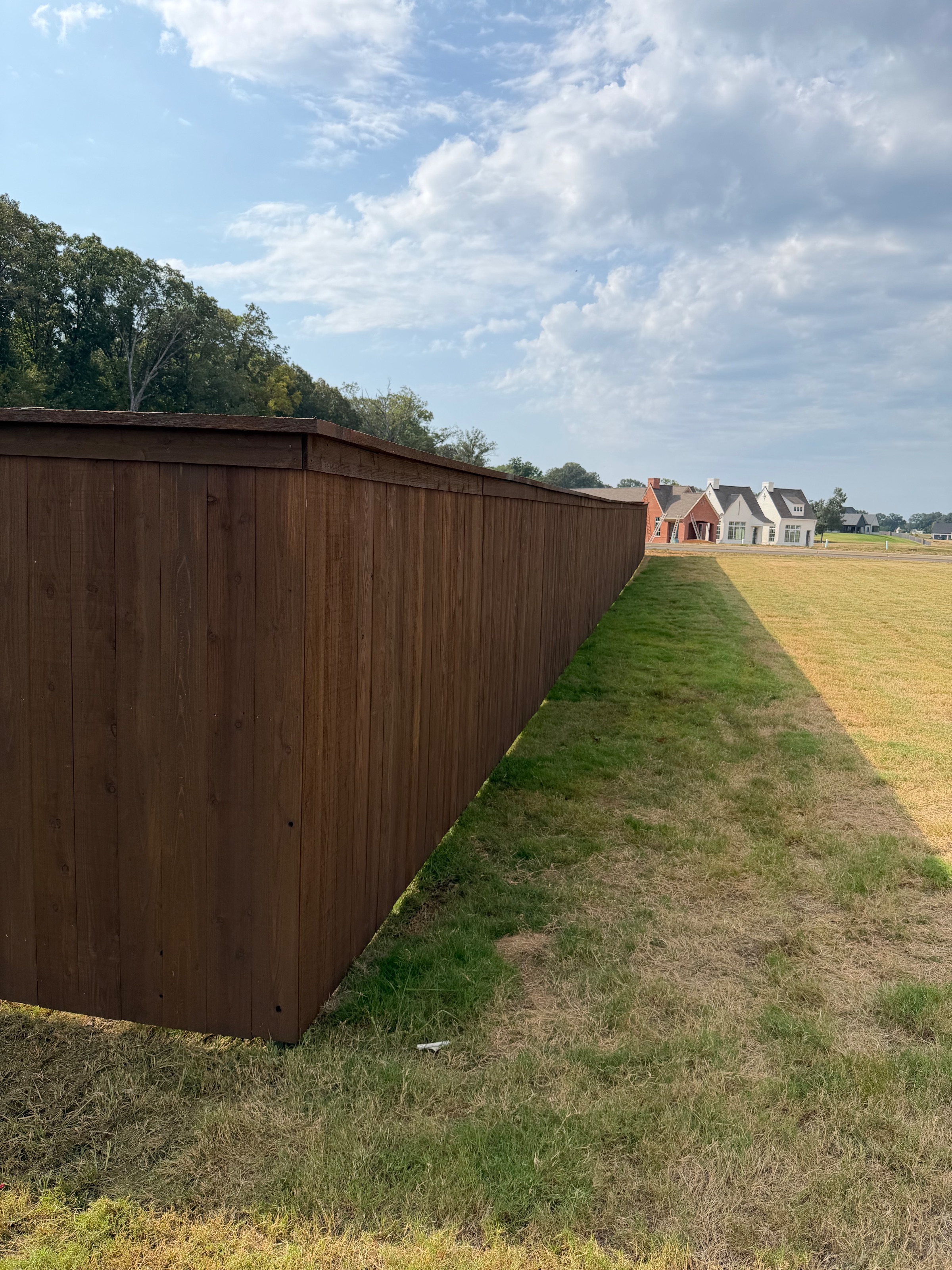 Pre-stained cedar privacy fence corner with a clean fence line across a sloping yard