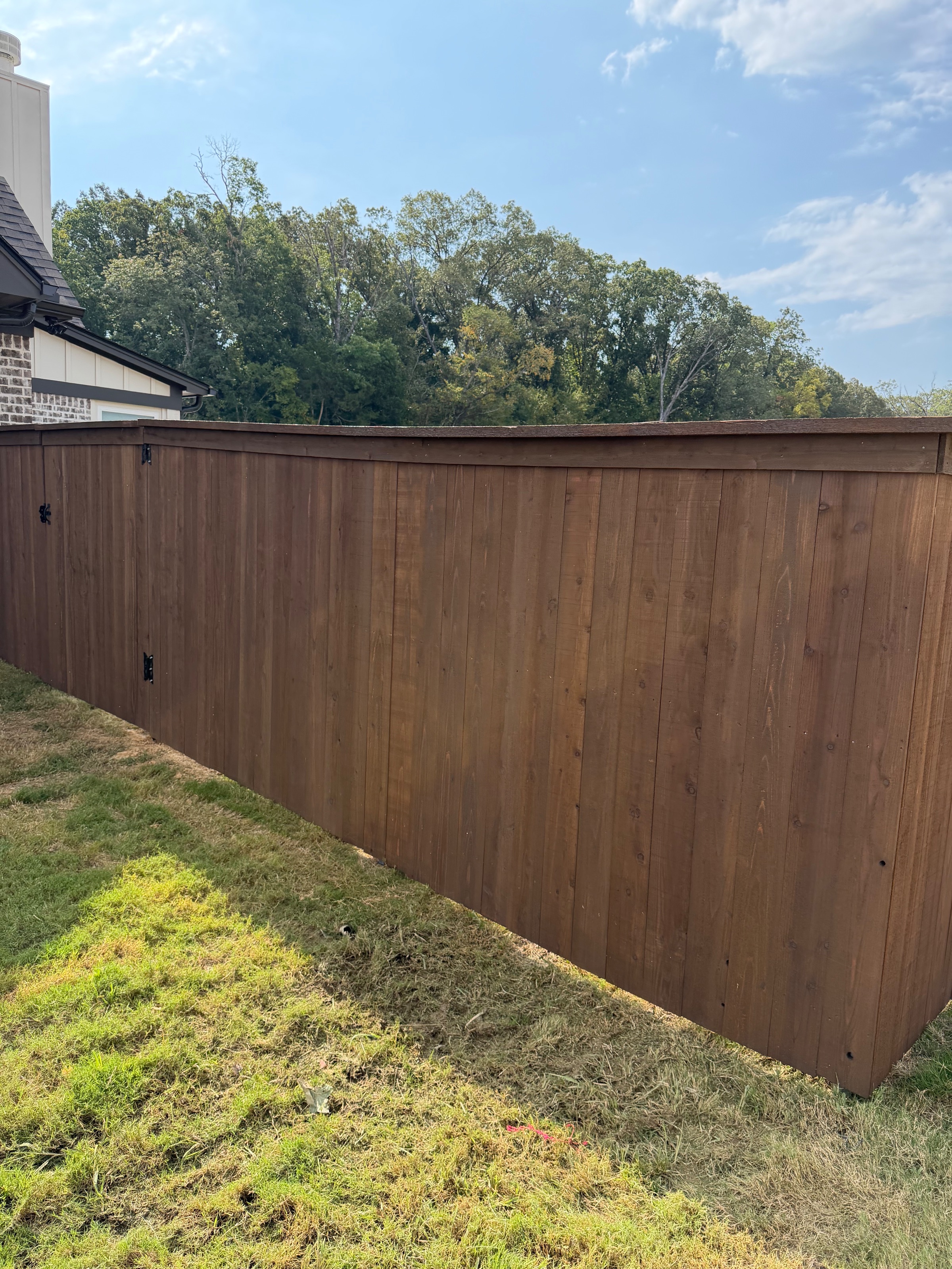 Finished side of a pre-stained cedar privacy fence along a tree line