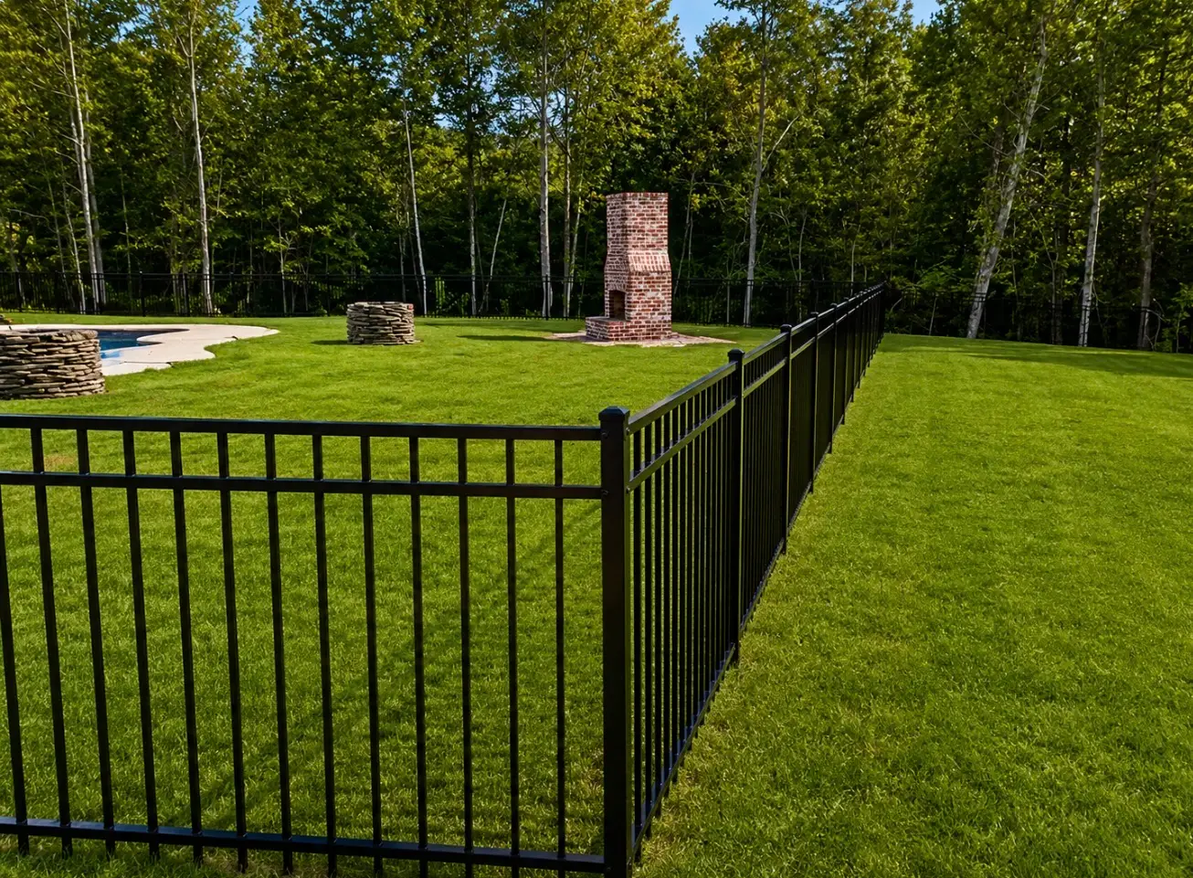 Black aluminum fence bordering a backyard pool and treeline